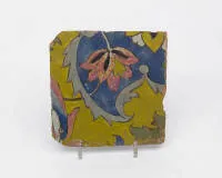 Safavid cuerda seca tile, Iran, second half 17th c., light red body, bubbly coloured glazes in yellow, cobalt blue, green and opaque purple, manganese outlines, 20.7 x 20.7 cm, edges chipped, some open glaze bubbles, especially in the purple.