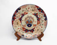 Grand plat mural, Japon, Arita, époque Meiji (1868-1912), fin du 19e siècle, porcelaine, style Imari décoré en bleu sous couverte, rouge de fer, vert et or, au centre un vase avec pivoines en fleurs et branches de saule sur une terrasse,...