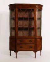 Sheraton display cabinet, England, circa 1900, satinwood and other veneers, ebonized string inlays, body with cylindrically curved sides and corresponding glazing, central door with pointed arch glazing bars, two drawers in lower third...