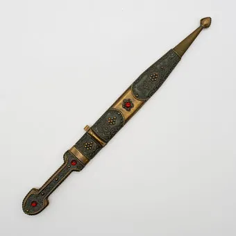 TRADITIONAL CAUCASIAN LONG DAGGER (KINDJAL), FROM THE CAUCASUS REGION, RICHLY DECORATED WITH ARTISTIC FLORAL PATTERNS AND DECORATIVE RED GLASS STONES, EARLY 20TH CENTURY.