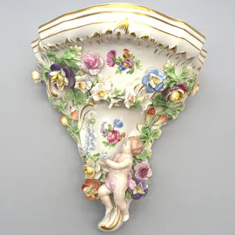SAXON PORCELAIN MANUFACTORY DRESDEN POTSCHAPPEL. WALL CONSOLE WITH PUTTO, RELIEF FLORAL DECOR AND GOLD DETAILS. EARLY 20TH CENTURY.