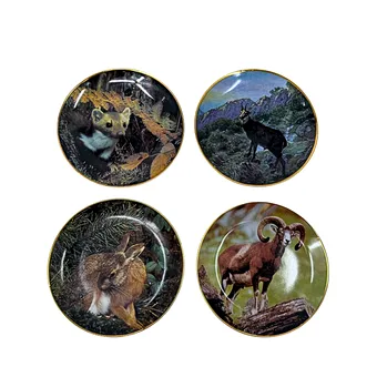 Four different collectible porcelain plates with gold rim and animal motifs.