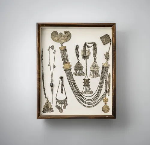 Groep sieraden, o.a. kettingen, hangers en riemen met oorbellen, deels van zilver, gemonteerd in twee vitrines