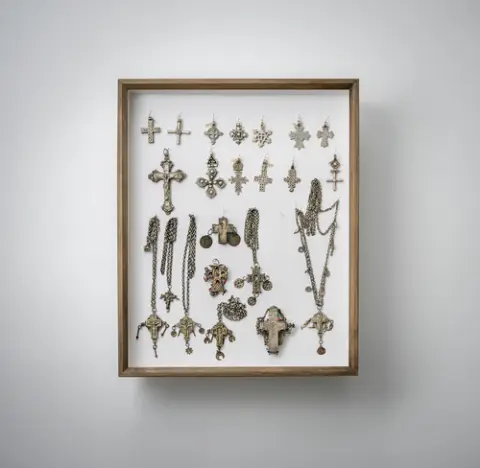 Groep riemgespen, hangers, kettingen en andere sieraden, deels van zilver, gemonteerd in twee glazen kasten
