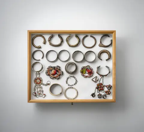 Groep armbanden, kettingen, hangers en amuletdoosjes, deels van zilver, gemonteerd in twee glazen kasten