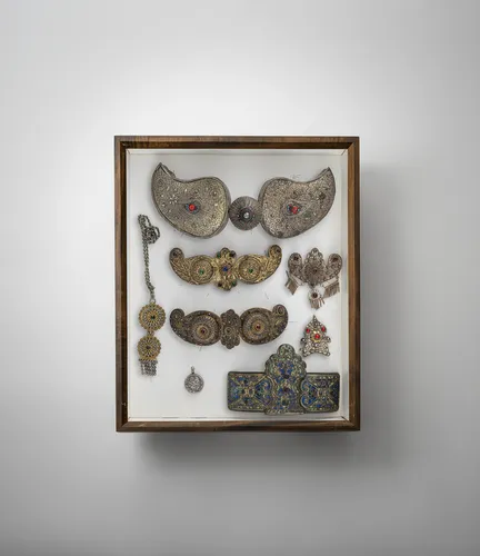 Group of 15 pieces, partly silver, with belt buckles, pendants and plaques mounted in two glass cases