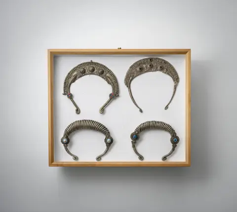 Groep van halssieraden, riem, betelsnijder en hangers, deels van zilver, gemonteerd in twee glazen kasten