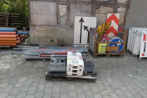 Lot of traffic signs and accessories, including guide beacons, barriers, base plates and sign posts, partly in mesh box