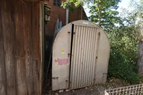 Corrugated sheet metal arched shelter with door, material storage