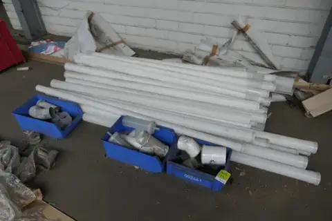 Zestaw artykułów sanitarnych m.in. ALMEVA, rury i kształtki, w plastikowych skrzynkach