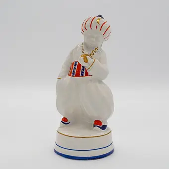 OSKAR BURKHARDT. FIGURA ORIENTALNA „TUREK”, ERNST TEICHERT GMBH (ZNANA RÓWNIEŻ JAKO CZĘŚĆ MIŚNIEŃSKIEJ FABRYKI PIECÓW I PORCELANY DAWNIEJ CARL TEICHERT), CHŁOPIEC W STROJU ORIENTALNYM, KAMIENINA, SZKLIWIONA, POLICHROMOWANA RĘCZNIE MALOWANA, CZĘŚCIOWO ZŁOCONA, OK. 1910.