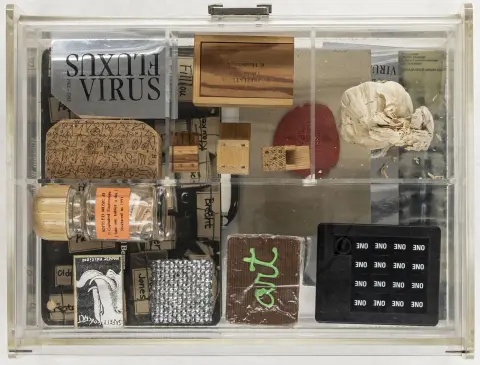 Fluxus – Samling av 10 objekter av ulike Fluxus-kunstnere. I akrylglassboks med uttakbar mellomplate med flere rom.