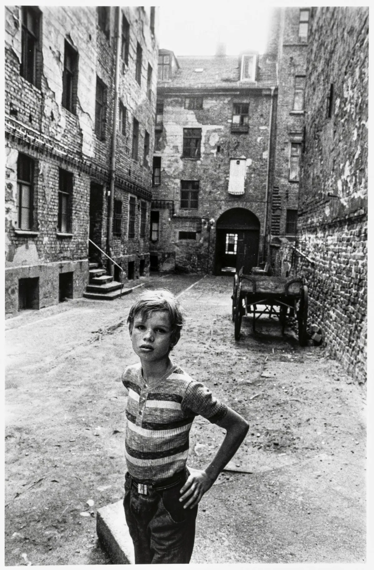 Höpker, Thomas – Untitled. (Boy in a run-down backyard). Original photograph. Silver gelatin (circa 1970). 27.5 x 18.5 cm.