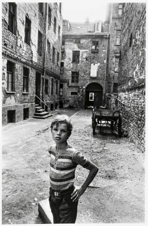 Höpker, Thomas – Bez naslova. (Dječak u zapuštenom dvorištu). Originalna fotografija. Srebrna želatina (oko 1970). 27,5 x 18,5 cm.…