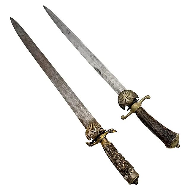 Deux couteaux de chasse avec manches en corne de cerf, décor de glands, rainures et garde en coquille, 19e/20e s.