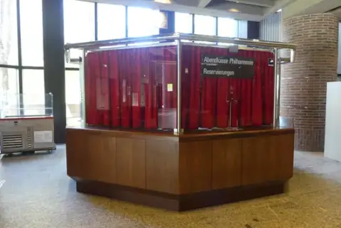 Pénztárpavilon/esti pénztár, sokszögű, fa burkolat üveg felépítéssel, rozsdamentes acél keretek és piros függönyök