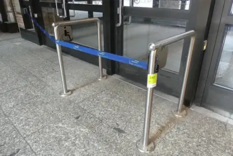 2 adet kişi yönlendirme sistemi/bariyer, zemine monte paslanmaz çelik kollar, kayış kasetleri ile