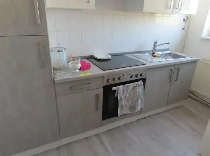 1 front de bucătărie încorporat, față gri cu blat și dulapuri suspendate, plită ceramică cu 4 zone integrată, cuptor și hotă, precum și chiuvetă cu zonă de scurgere și frigider încorporat