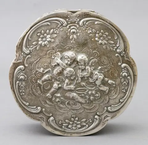 Boîte, argent 800, allemande, Wilhelm Weinranck & Fritz Schmidt, Hanau, 3e rococo, 1900 - 1950 décor de fleurs, roses, rocailles et nombreux putti, certains musiciens. Couvercle à charnière. D 16 cm, H 6,3 cm, poids 400 g. Poinçonné au fond : 800, croissant, couronne et poinçon de maître WSH dans un cœur.