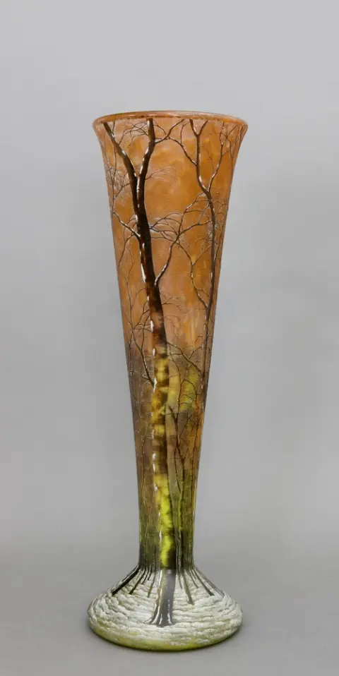 Vase, Daum Frères, Nancy, France, début 20e s. Vase en verre en forme de trompette sur pied rond évasé. Décor camée (gravé et émaillé) avec arbres dans un paysage d'hiver sur ciel orange. H 49,5 cm. Au fond, gravé "Daum Nancy".