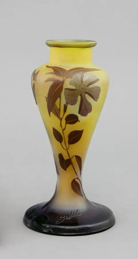 Vase, Emile Gallé, Nancy, France, vers 1910. Verre blanc laiteux avec sous-couche/surcouche violet/jaune, décor gravé en relief d'une fleur avec feuilles et fleurs ainsi que papillons. Vase à épaulement. Base ronde légèrement montante, panse élancée en balustre et col court. H 16,5 cm. Sur la base, signé en relief Gallé.